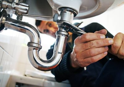 man turning a pipe under a sink with a special tool