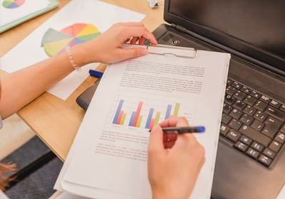 Personne annotant un document imprimé avec des graphiques à côté d'un ordinateur portable.