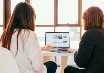 two women sitting at a table with a laptop