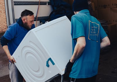 a man in a blue shirt is moving a refrigerator