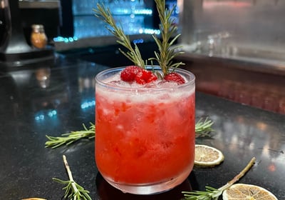 a cocktail with a sprig of rosemary on the side of a bar