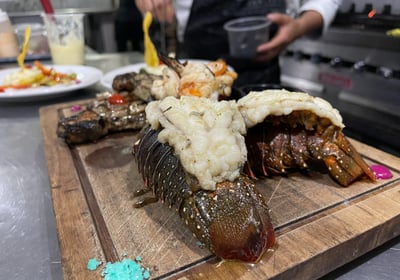 a lobster tail on a cutting board with a chef in the background