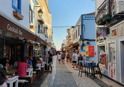Charming cobbled street in Alvor lined with lively bars, shops, and colorful storefronts.