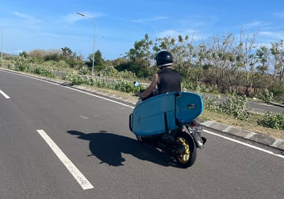 a man riding a scooter with a surfboard