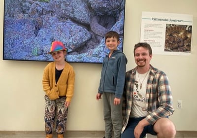 Project Rattlecam Team member, Owen, and 2 kids in front of RattleCam Zoo display