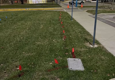 Utility flags and paint marking the location of an underground utility to an inground utility box.