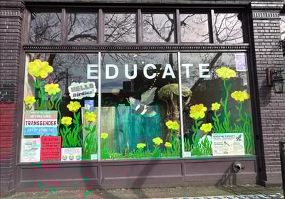 Large storefront window with the word EDUCATE printed on top of large painted yellow flowers