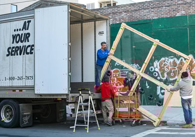 Four people lifting a large window out of a moving truck