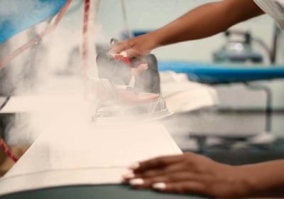 A person pressing an iron on fabric with steam rising in a laundry room.