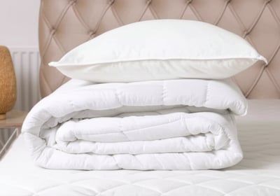 Stacked white pillows and comforter on a bed with a padded headboard.
