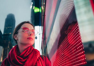 a woman in a red scarf and glasses next to led screen