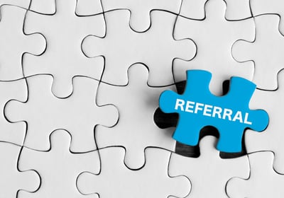 white puzzle with one blue piece with the word "referral" printed on it
