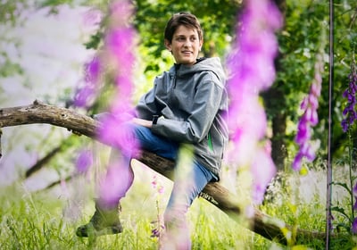 Der junge Naturfotograf Philipp Geisler sitzt auf einem Ast, im Vordergrund Wildblumenblüten