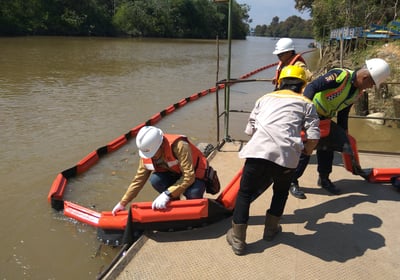 a group of people in safety vests and helmets on a boat deploy oil boom in river