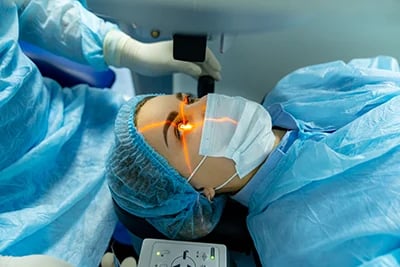 Paciente em sala cirúrgica realizando procedimento oftalmológico a laser com uso de touca e máscara