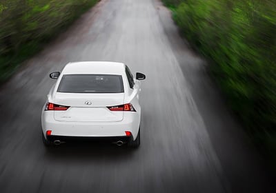 a white car driving down a road with trees in the background