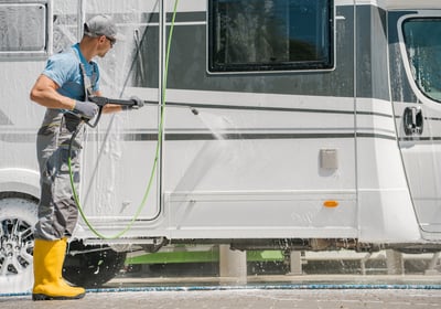 A man in yellow boots is pressure washing an RV