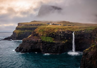 a waterfall falls down a cliff into a body of water. Gásadalur Múlafossur in the Faroe Islands