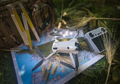 Drone, controller, landkaart en meetgereedschap liggen klaar op gras voor terreinverkenning en luchtinspectie