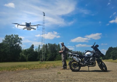 Drone stijgt op voor inspectievlucht terwijl piloot toezicht houdt, naast adventuremotor op open terrein