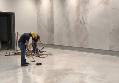 An interior space featuring a modern showroom with large ceramic tiles and bright lighting. The walls display brand signage and various tile samples. A sleek, minimalist desk is centered, surrounded by a clean and spacious environment.