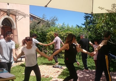 a group of people holding hands and dancing in a garden, classe di bioenergetica