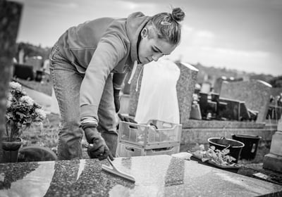 Personne nettoyant une pierre tombale avec une raclette dans un cimetière