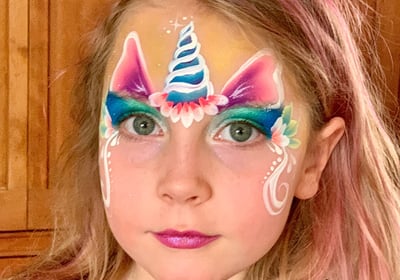 a young girl with a floral unicorn face paint on her face