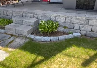 grey brick patio on the rear of a house with steps made of stone with manicured lawn