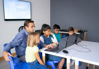 Instructor guiding kids in a small group tech class with laptops