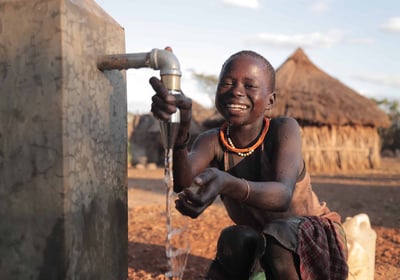 Smiling child drinking clean water from a well in a rural African village