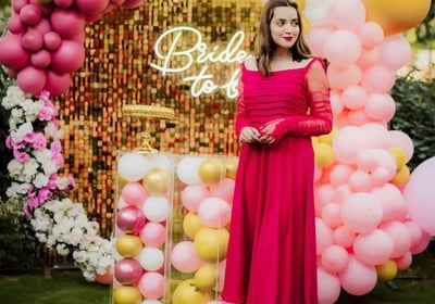 a woman in a red dress standing in front of a pink and gold balloon filled