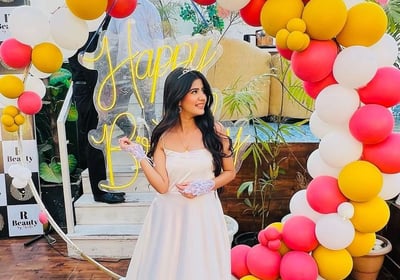 a woman in a white dress standing in front of a large arch shaped balloon