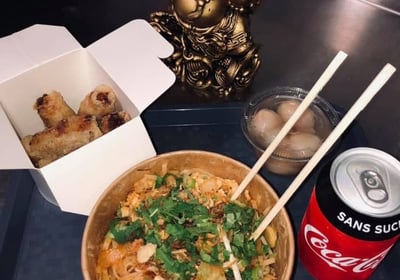 a bowl of noodles with chopsticks and a soda can be seen