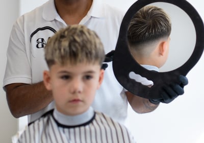 Kid having the back of his head shown through a mirror within a mirror to show a haircut