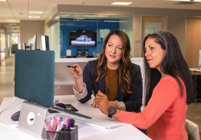 two women sitting at a desk with a laptop