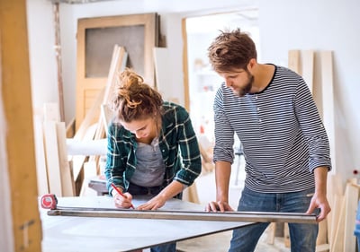 Une femme et un homme en train de mesurer une planche de bois