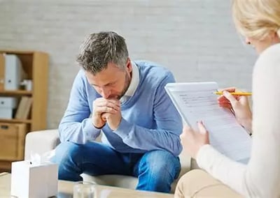 Femme aidante écoute un homme penché en avant coudes sur ses cuisses