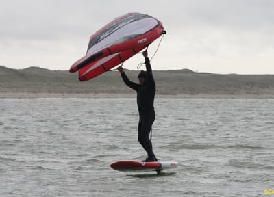 Un homme tient sa wing sur sa planche de wingfoil
