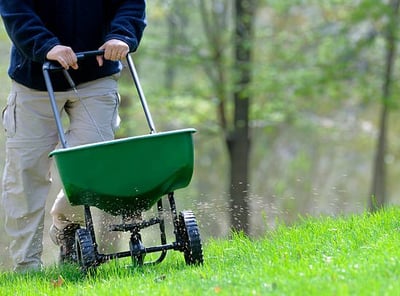 a man is walking in the grass with a lawn spreader