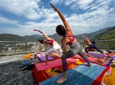 Person practicing yoga asanas outdoors with a scenic view of the Himalayan mountains in the background.