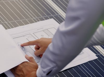 um homem de camisa social apontando um desenho técnico sobre um módulo fotovoltaico