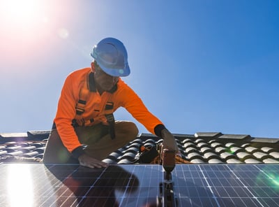 um instalador no telhado fixando um módulo fotovoltaico com uma parafusadeira