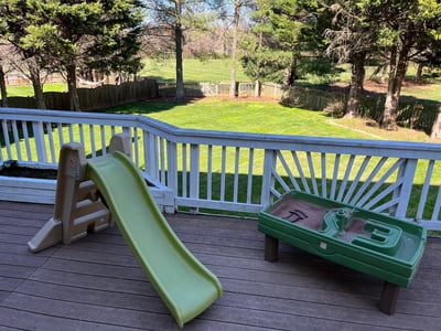 Photo of outdoor play area with sand pit and green slide.