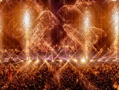 un concert avec un grand groupe de personnes et une scene avec des machines à étincelles