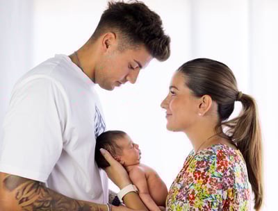 Sessió de fotos newborn a Girona amb una bebè dormint als braços dels pares en estudi fotogràfic