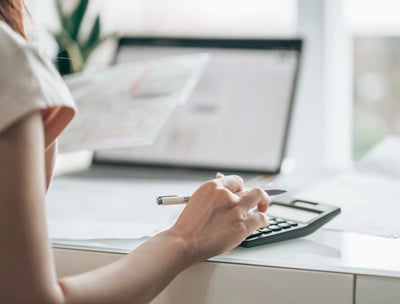 Woman managing monthly bookkeeping, using a calculator and computer to organize financial records.