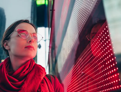 a woman in a red scarf and glasses next to led screen