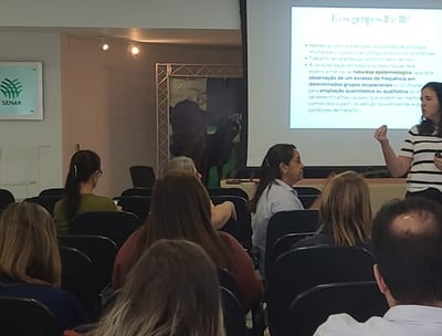 Foto de mulher psicóloga apresentando palestra sobre saúde mental para plateia empresarial.