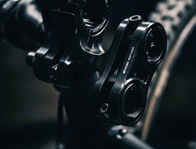 A close-up, darkly lit photograph of specialized bike mounts, crafted from dark, possibly anodized metal. The focus is on the